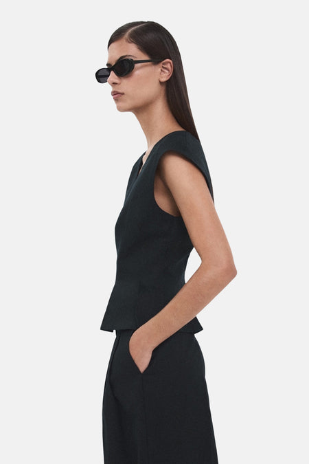 Chemisier sans manches bleu foncé de MANGO, porté avec un pantalon assorti et des lunettes de soleil ovales.
