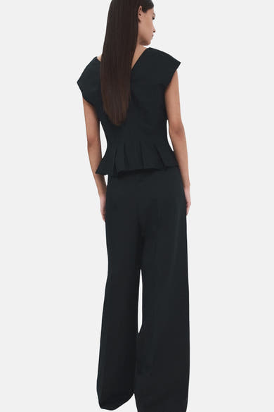 Blouse bleu foncé sans manches de MANGO, coupe peplum, détail de plis et pantalon taille haute porté.
