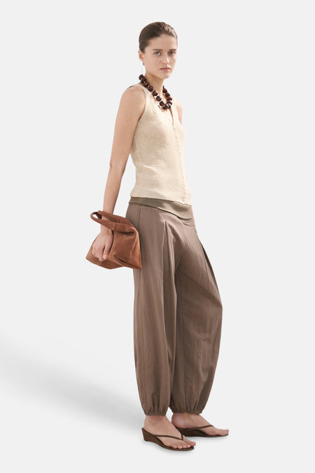 Top sans manches beige de MANGO, porté avec un pantalon bouffant marron et un collier de perles.
