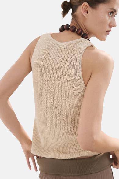 Top sans manches beige de MANGO, en maille fine, porté avec un collier à grosses perles.