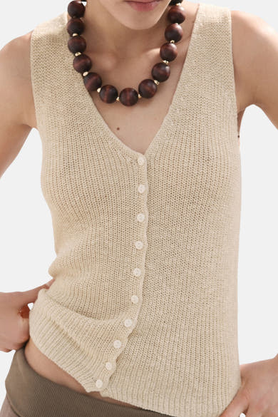 Beige mouwloze top van MANGO, met knoopsluiting aan de voorkant en bruine parelketting.