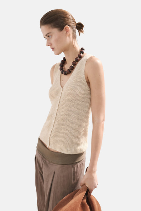 Top sans manches beige de MANGO, porté avec un pantalon marron et un collier de perles en bois.