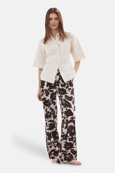 Pantalon fleuri multicolore de MANGO, à jambes larges, porté avec une chemise écrue.