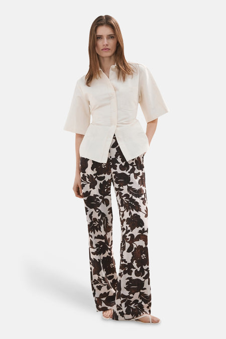 Pantalon fleuri multicolore de MANGO, à jambes larges, porté avec une chemise écrue.