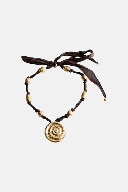 Bruine MANGO-ketting met gouden spiraalhanger en gouden kralen, gedragen door een vrouw.