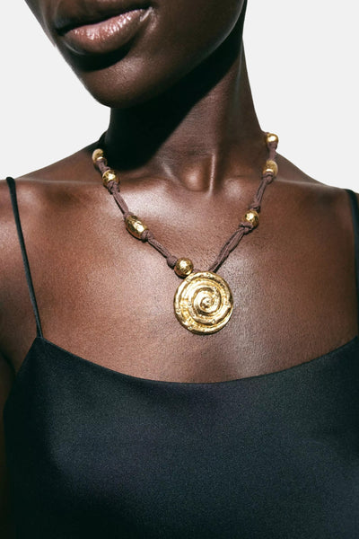 Collier brun de MANGO avec pendentif spirale doré et perles dorées, porté par une femme.