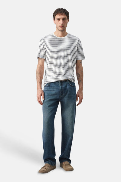 Multicolored striped short-sleeve t-shirt with white base and thin navy horizontal stripes, worn by model in full-length front view with blue jeans and brown loafers.