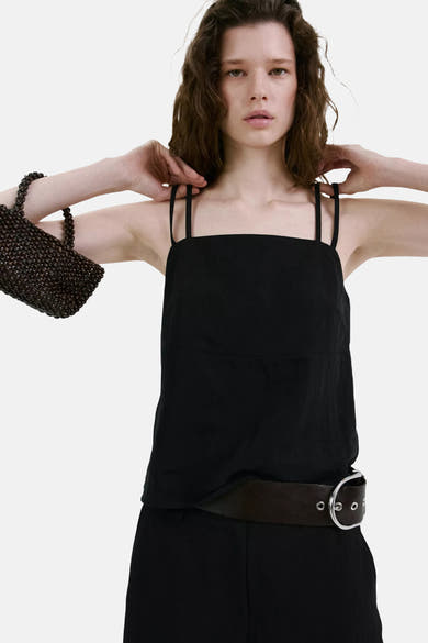 Top noir à fines bandes de MANGO, porté avec un pantalon noir, une ceinture marron et un sac perlé.