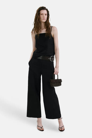 Top noir à fines bretelles de MANGO avec encolure droite, porté avec un pantalon large et une ceinture.