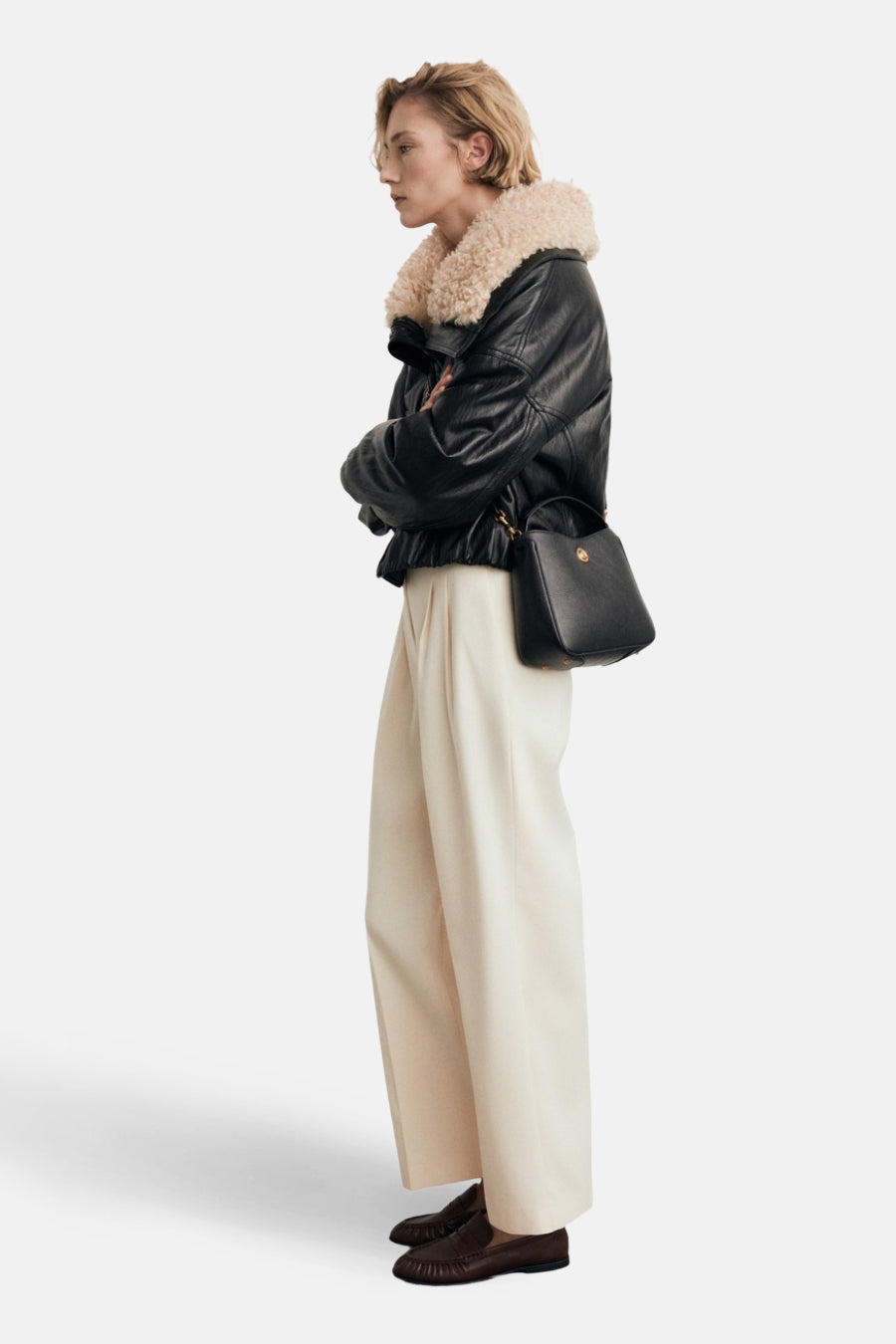 Beige schoudertas van MANGO, gedragen met een zwart leren jack en een broek met hoge taille.