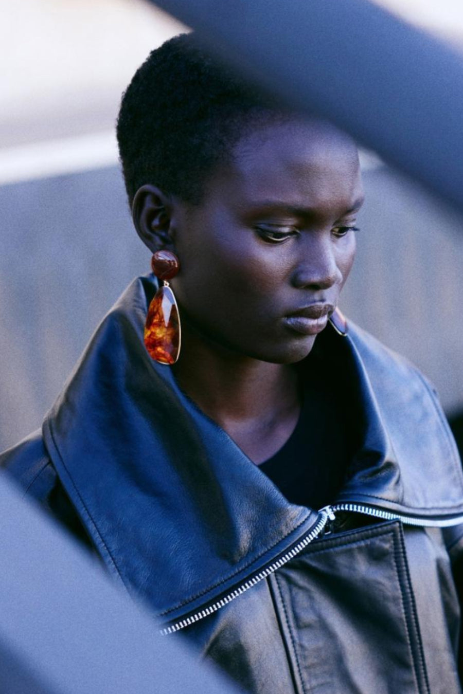 Boucles d'oreilles pendantes marron de MANGO, portées avec une veste en cuir noire.