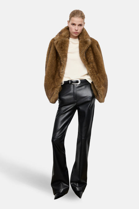 Chemisier écru à manches longues de MANGO, porté avec un manteau en fausse fourrure marron et un pantalon noir en similicuir.