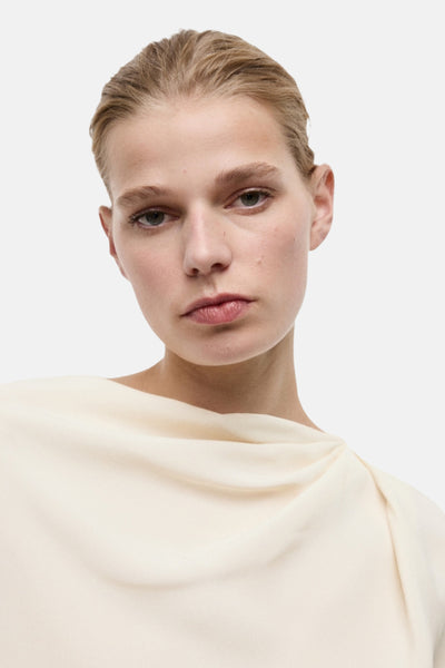 Ecru blouse met lange mouwen van MANGO, delicate draperie bij de halslijn, op een lichte effen achtergrond.