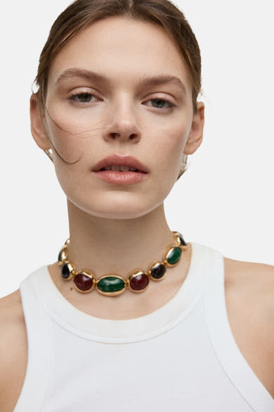 Korte, meercleurige halsketting van MANGO, versierd met rode, groene en zwarte steenen, gedragen met een witte crop top.