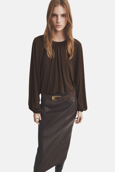 Blouse marron à manches longues de MANGO, avec un col froncé et portée avec une jupe en cuir et une ceinture.
