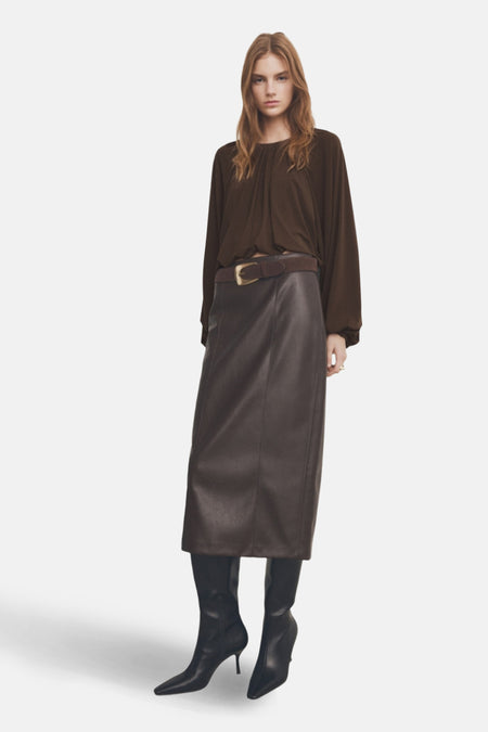 Chemisier à manches longues brun de MANGO, porté avec une jupe en similicuir marron et des bottes noires.
