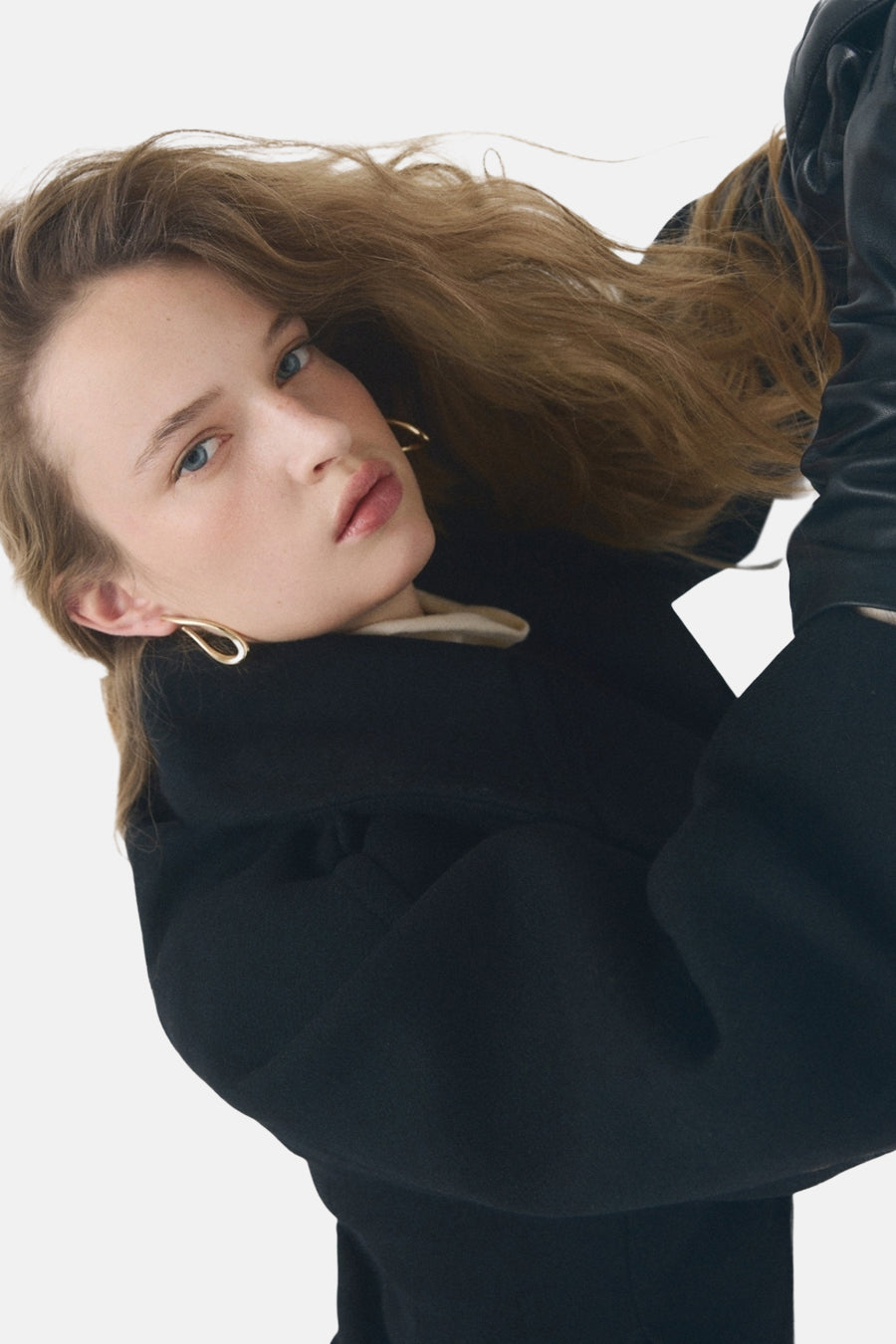 Boucles d'oreilles dorées de MANGO, design en forme de goutte, portées avec un manteau noir et des gants en cuir.