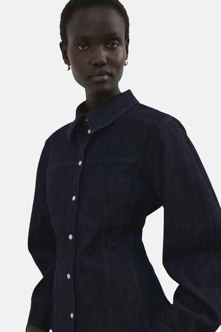 Chemise à manches longues en denim bleu foncé de MANGO, avec boutons blancs et coupe ajustée.
