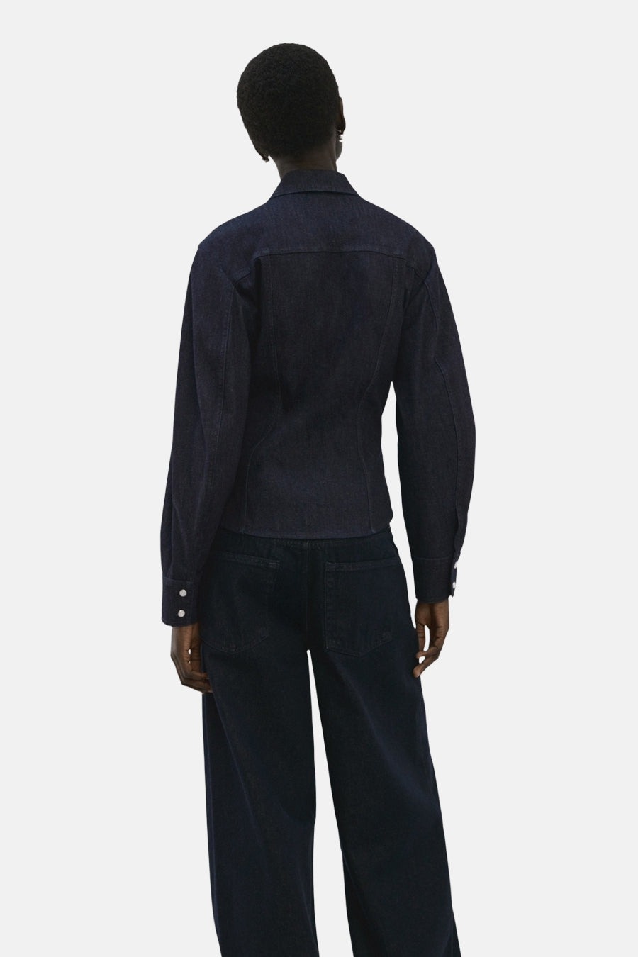 Chemise à manches longues en denim bleu foncé de MANGO, vue de dos, portée avec un pantalon assorti.