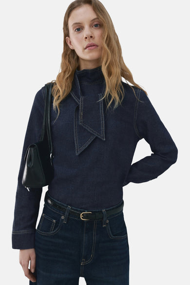 Chemisier denim bleu marine à manches longues de MANGO, avec cravate décorative et porté avec un jean et un sac à main noirs.