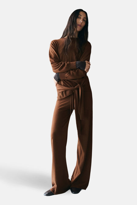 Pantalon brun de MANGO, coupe ample avec une ceinture nouée, porté avec un pull assorti et des chaussures noires.