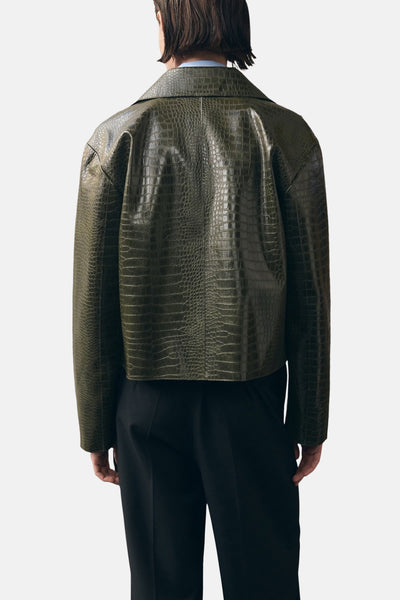 Veste courte kaki par MANGO, à motif crocodile, portée avec un pantalon noir.