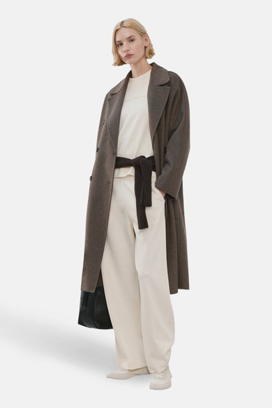 Jogging beige de MANGO, porté avec un pull blanc, un manteau marron et une ceinture marron nouée.