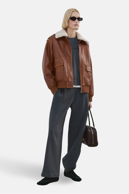 Jogging bleu de MANGO, porté avec une veste en cuir marron à col en fausse fourrure.