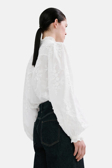 Blouse à manches longues blanche de MANGO avec broderie florale, manches bouffantes et détails à volants.