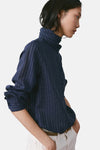 Blauwe blouse met lange mouwen en strepen van MANGO, met een strik op de rug, gedragen met een witte broek en een bruine riem.