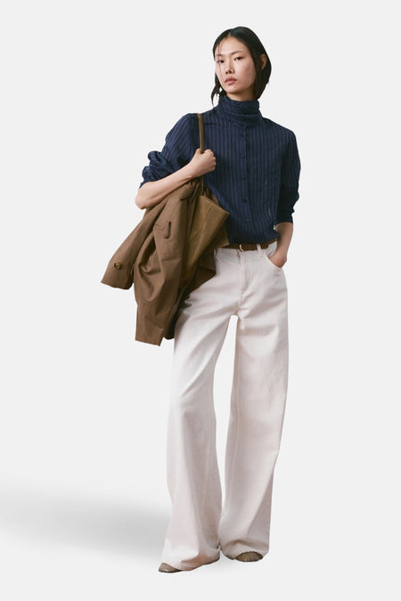 Blouse à manches longues bleue rayée de MANGO, portée avec un jean blanc taille haute et une veste marron.
