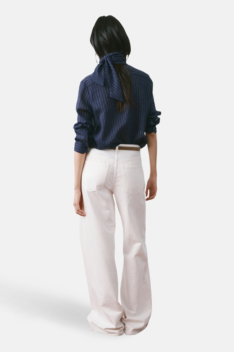 Blouse à manches longues bleue à rayures by MANGO, avec un nœud au dos, portée avec un pantalon blanc et une ceinture marron.