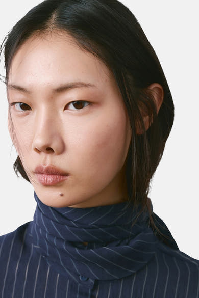 Blauwe blouse met lange mouwen van MANGO, verticale strepen op een marineblauwe achtergrond, gedragen door een model.
