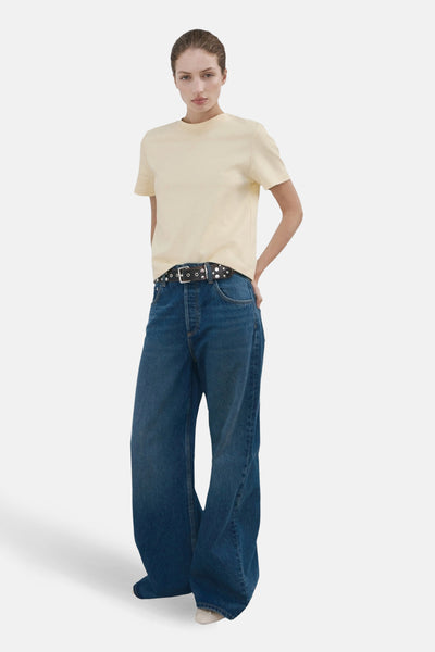 T-shirt jaune à manches courtes de MANGO, porté avec un jean ample et une ceinture cloutée.