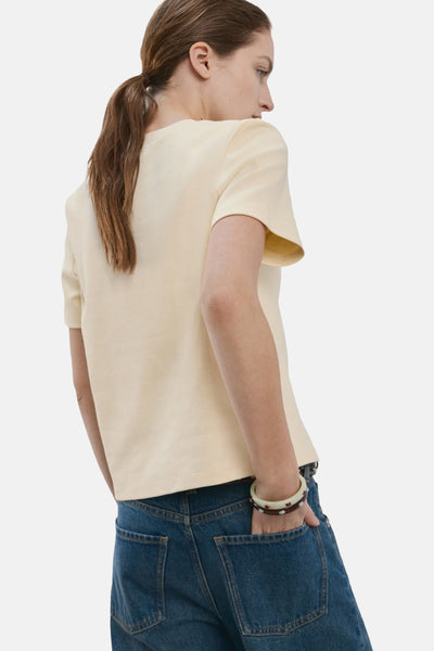 T-shirt jaune à manches courtes de MANGO, porté avec un jean bleu et des bracelets décoratifs.