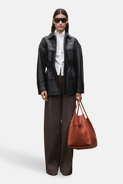 Chemise à manches longues blanche de MANGO, portée avec une veste en cuir noire, un pantalon marron et un sac à main en cuir marron.
