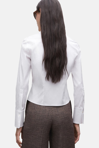 Chemise à manches longues blanche de MANGO, vue de dos, portée avec un pantalon marron texturé.

