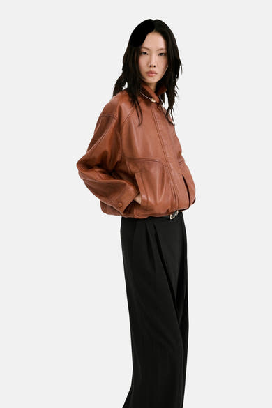 Zwarte broek van MANGO, wijd en geplooid, gedragen met een bruin leren jasje en een riem.
