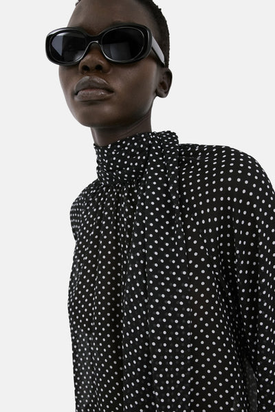 Blouse noire à pois, de MANGO, avec col montant et manches longues bouffantes.
