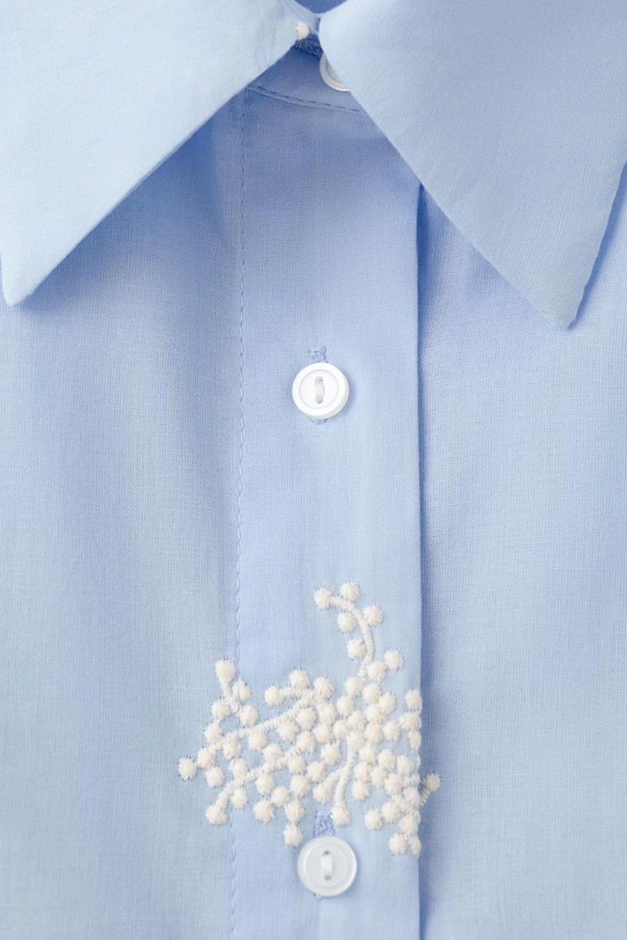 Blauwe blouse met lange mouwen van MANGO, met witte bloemenborduursel op de knoopsluiting.