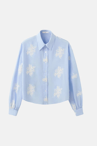 Blauwe blouse met lange mouwen van MANGO, versierd met witte geborduurde bloemenpatronen.