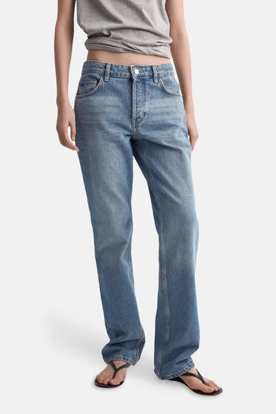 Middelblauwe bootcut jeans van MANGO, gedragen met een geknoopt grijs T-shirt.