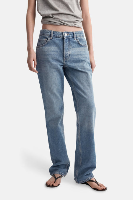 Jean bootcut en denim bleu moyen de MANGO, porté avec un t-shirt gris et des sandales.