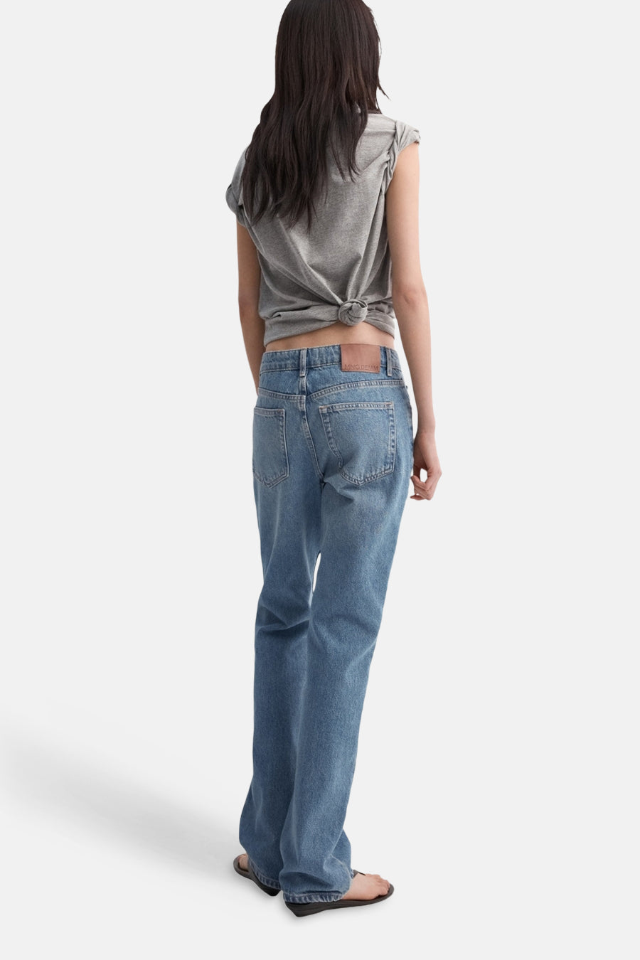 Jean bootcut bleu moyen de MANGO, porté avec un t-shirt gris noué.