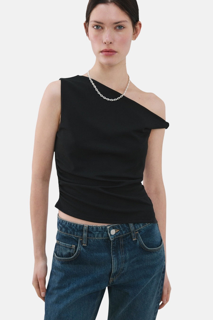 Top noir sans manches de MANGO, porté avec un collier argenté et un jean taille basse.
