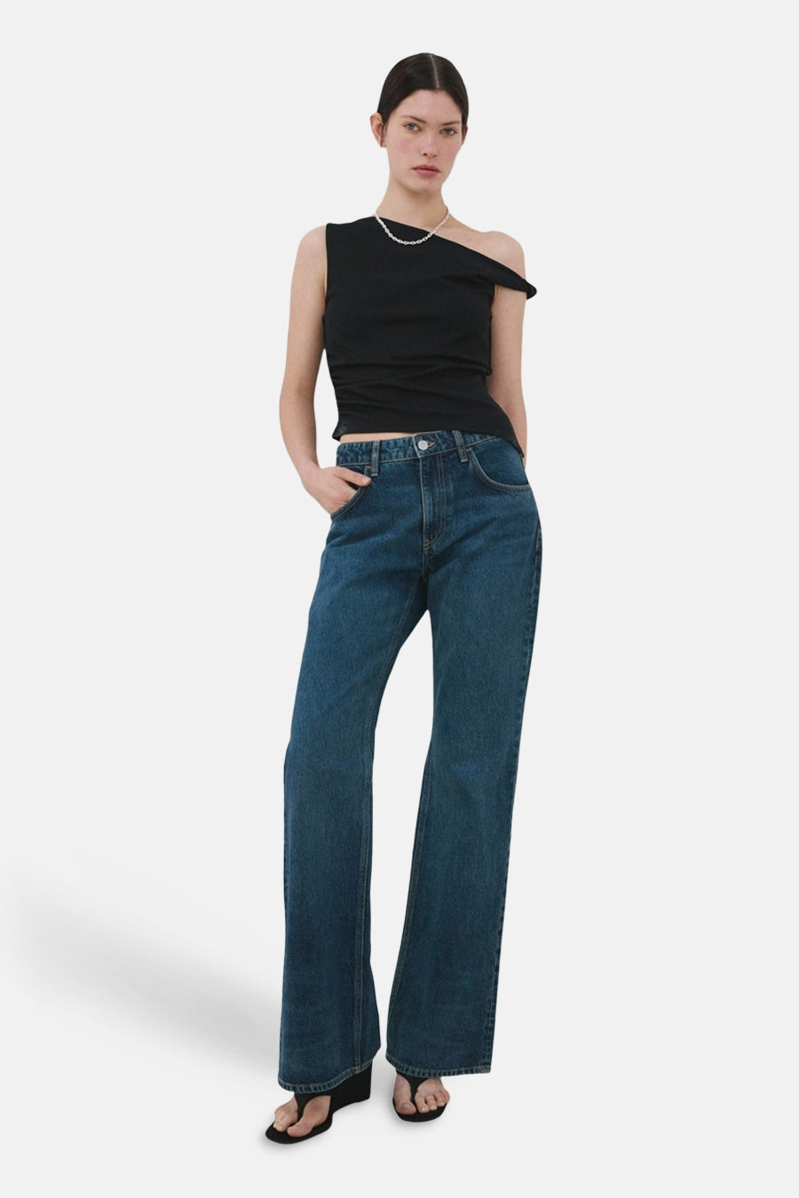 Top noir sans manches de MANGO, porté avec un collier de perles et un jean bleu ample.