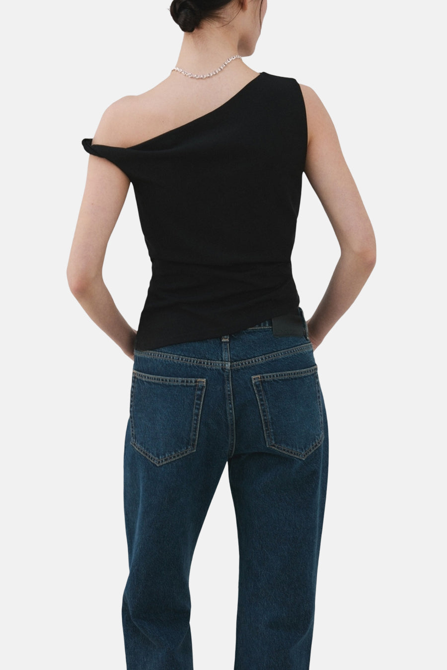 Top noir sans manches de MANGO, porté avec un collier argenté et un jean bleu taille haute.