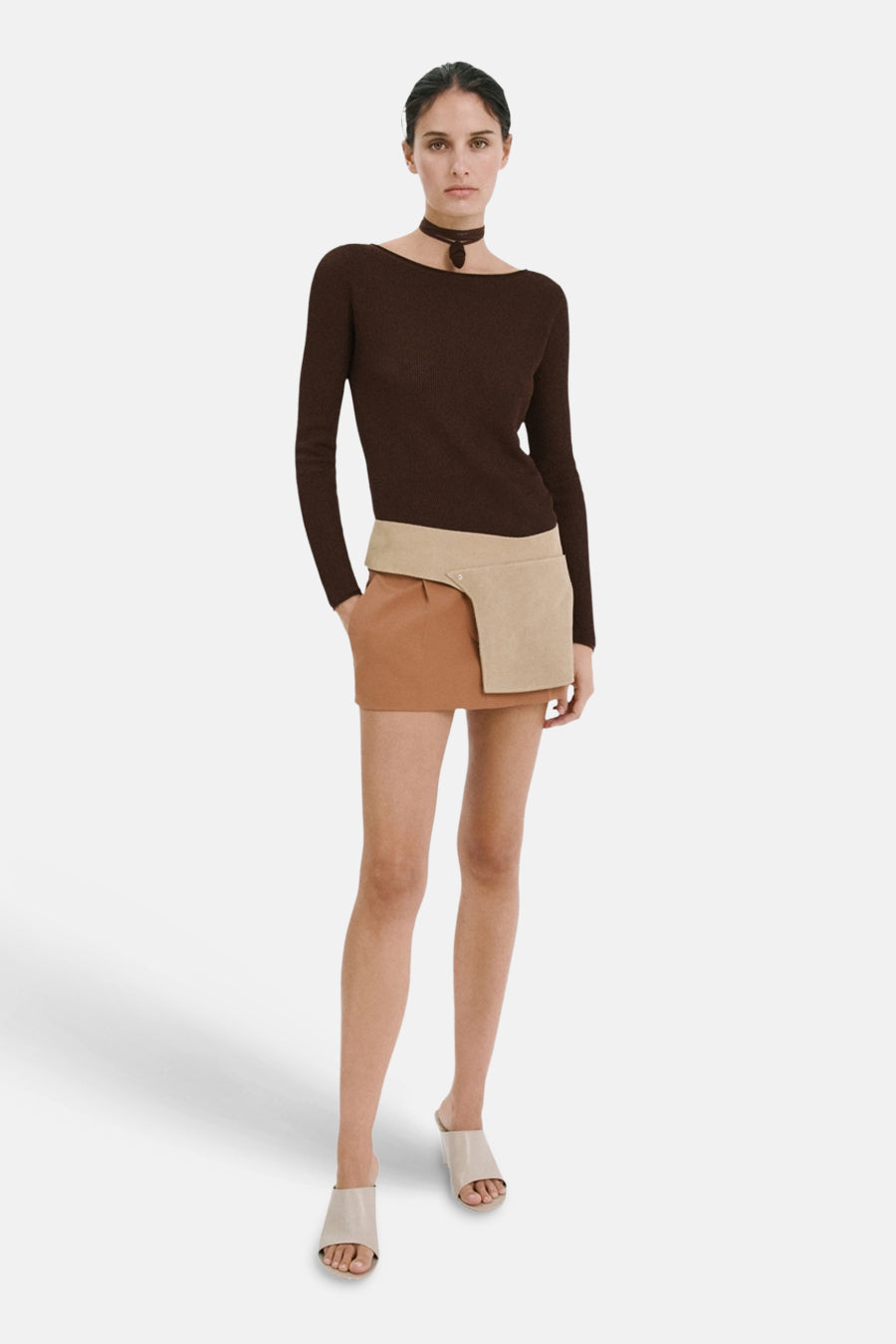 Pull brun en maille côtelée de MANGO à col bateau, porté avec une mini-jupe bicolore et des mules claires.