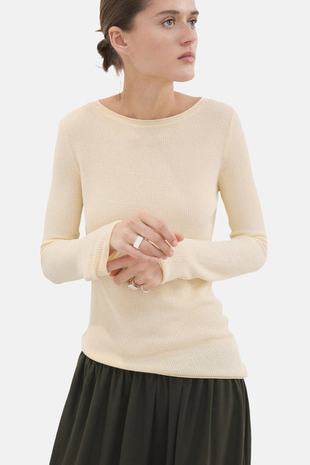 Pull col O jaune texturé en maille gaufrée de MANGO, à manches longues, porté avec une jupe foncée et des bagues.