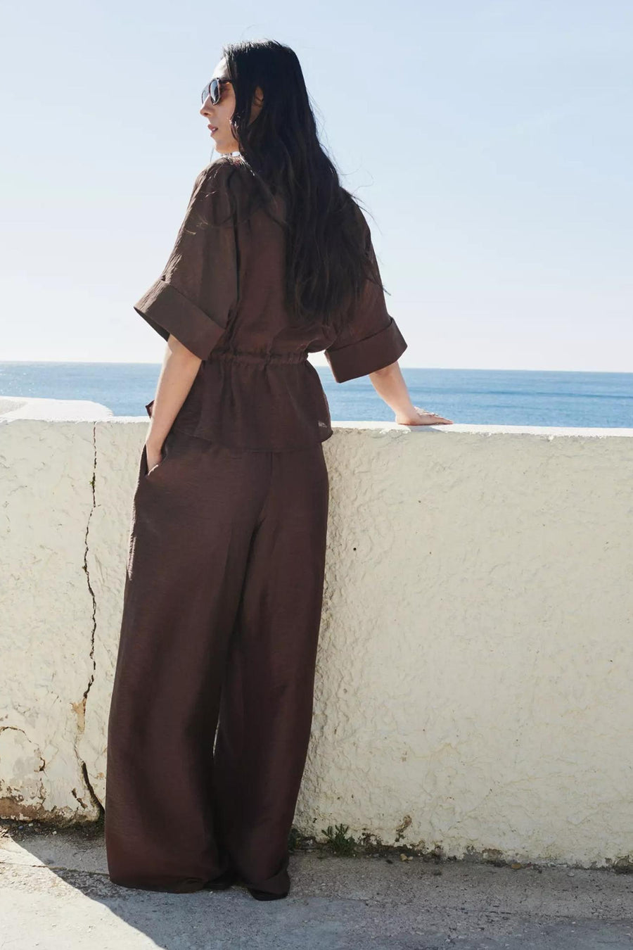 Blouse brune de MANGO à manches courtes retroussées et taille élastiquée, portée avec un pantalon assorti.